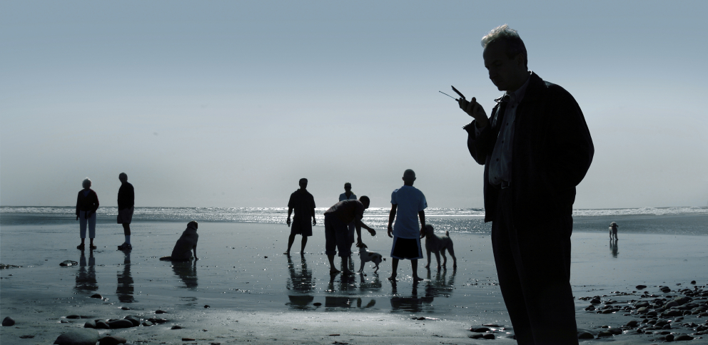 Man with mobile phone at beach Man with mobile phone at beach with people and dogs in background